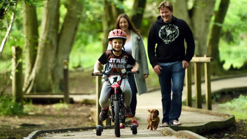 Family walking and cycling with a dog along a boardwalk through Hatfield Forest, Essex